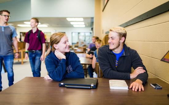 Students seated at a table at M州 smile at each other