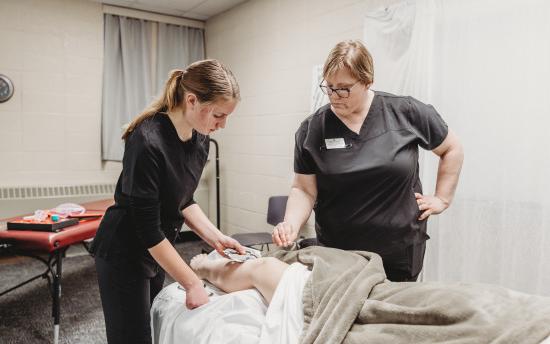 A massage therapy student and her instructor practicing massaging a leg