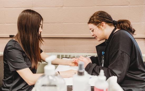 A student is practicing a manicure on another student